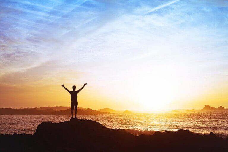 man with arms wide standing on a rock at sunset at the beach