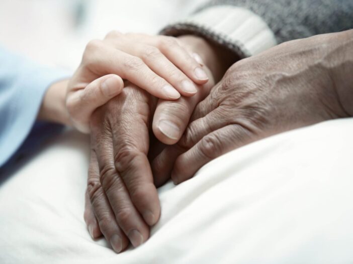 young and old hands holding each other in a hospital bed