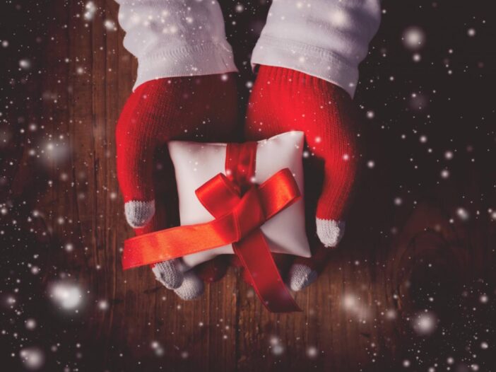 person with red gloves giving a white gift box and red ribbon
