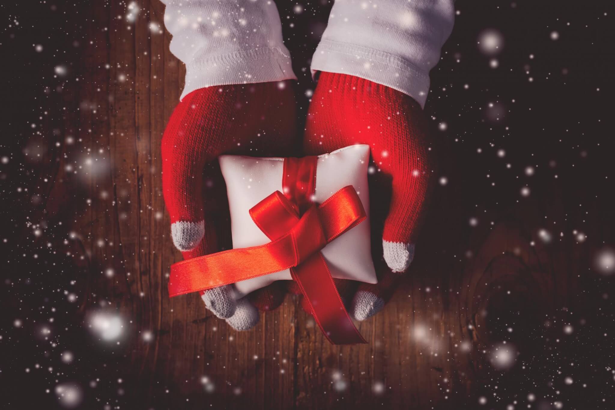 person with red gloves giving a white gift box and red ribbon