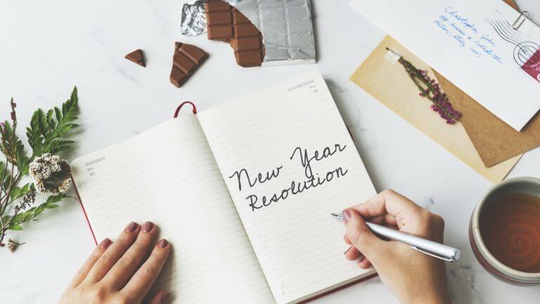 person writing in a notebook with the words New Year Resolution