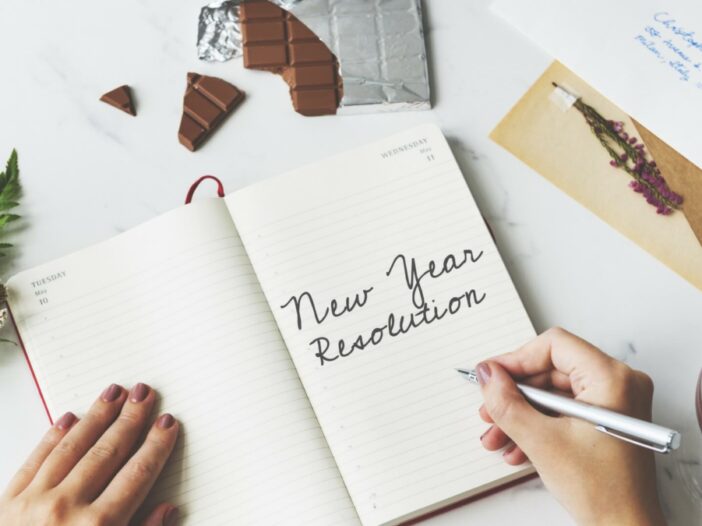 person writing in a notebook with the words New Year Resolution