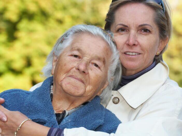 older mother and daughter hugging and smiling at the camera