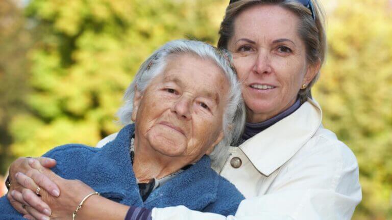 older mother and daughter hugging and smiling at the camera