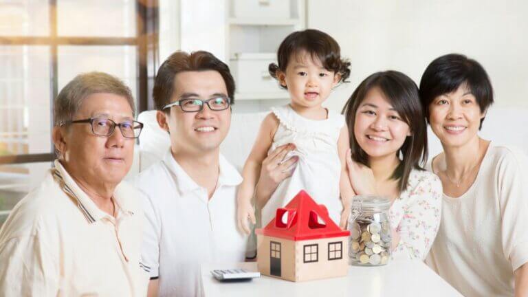 multigenerational family smiling with small house and coins on table