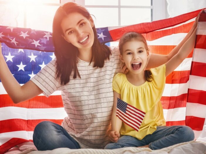 smiling mom and daughter with American flag held up behind them