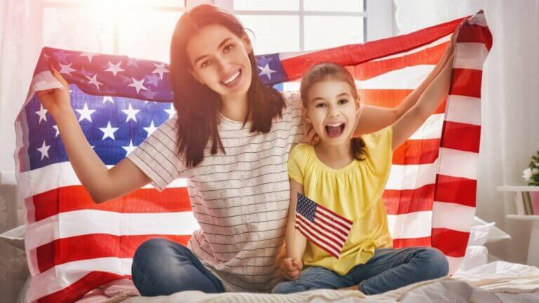 smiling mom and daughter with American flag held up behind them