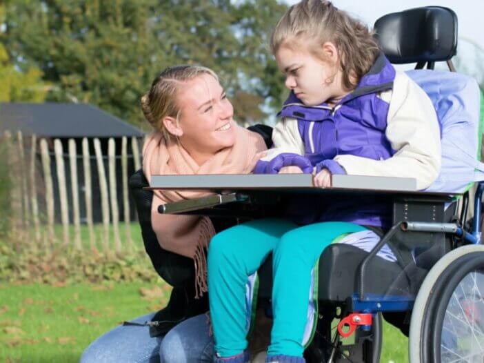 smiling caregiver and a young person with special needs in a wheel chair