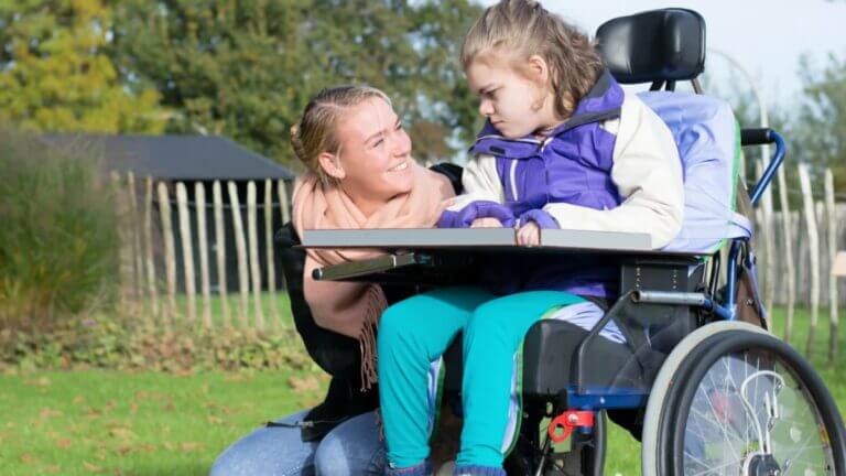 smiling caregiver and a young person with special needs in a wheel chair