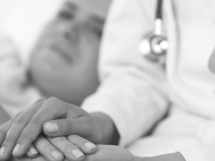 close of doctor's hand's consoling patient in the background out of focus
