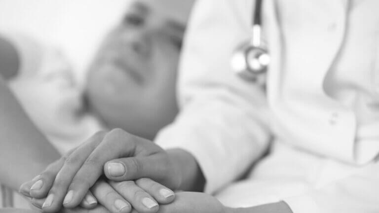 close of doctor's hand's consoling patient in the background out of focus