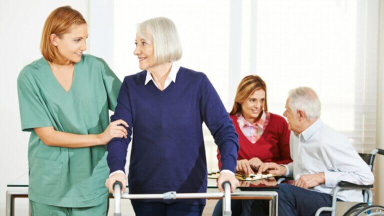 older woman with walker and nurse looking at each other, older man playing chess with women in the back