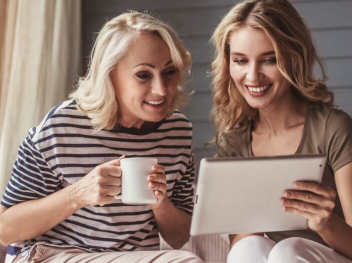 daughter and mom smiling with cup of coffee looking at an i pad