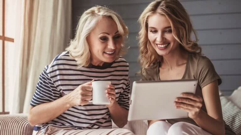 daughter and mom smiling with cup of coffee looking at an i pad