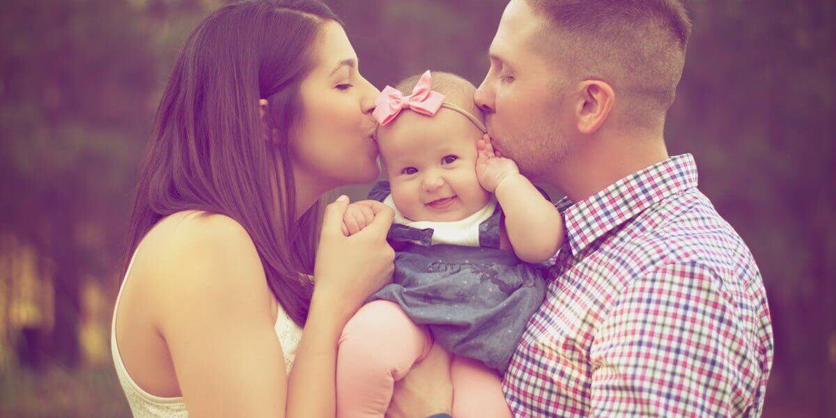 young couple kiss their smiling baby