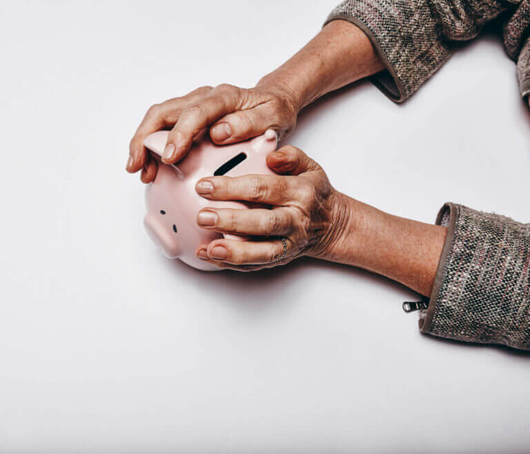 Top view of senior woman hands holding a piggy bank on grey surface