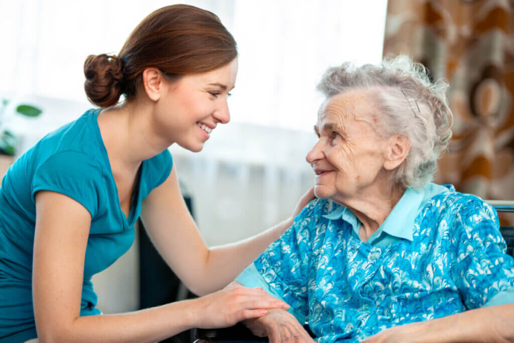 Elderly woman and her smiling caregiver or grand daughter smile at each other