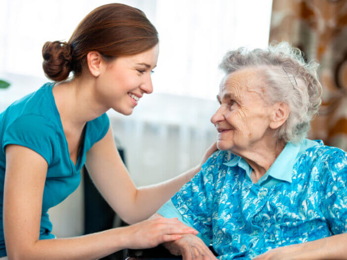 Elderly woman and her smiling caregiver or grand daughter smile at each other