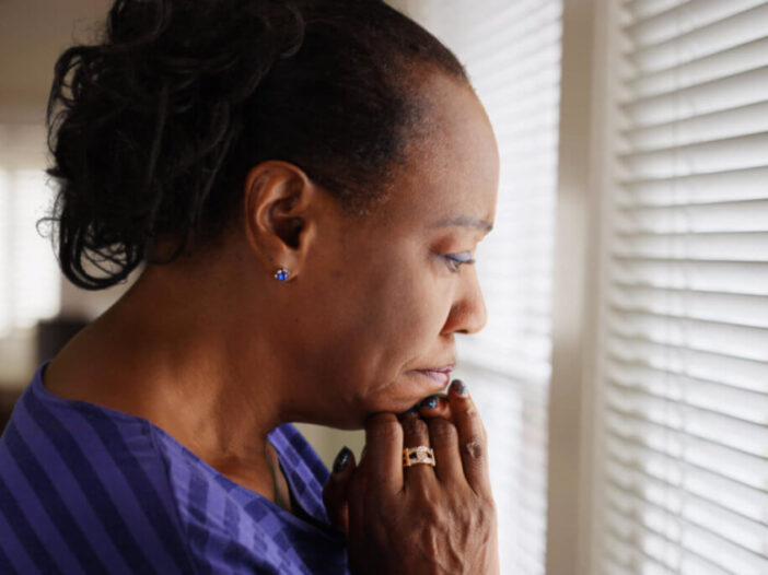 An older black woman mournfully looks out her window