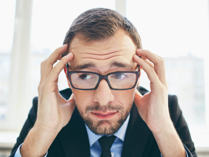 Frustrated businessman in eyeglasses touching his head