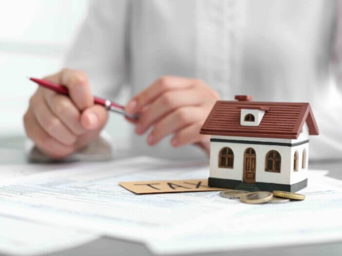 House model, coins and blurred woman on background. Tax day