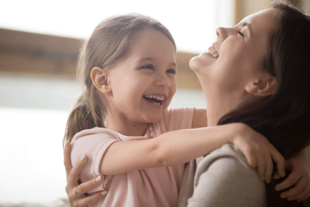 Cute kid girl and smiling mom laughing embracing cuddling together