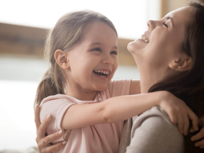 Cute kid girl and smiling mom laughing embracing cuddling together