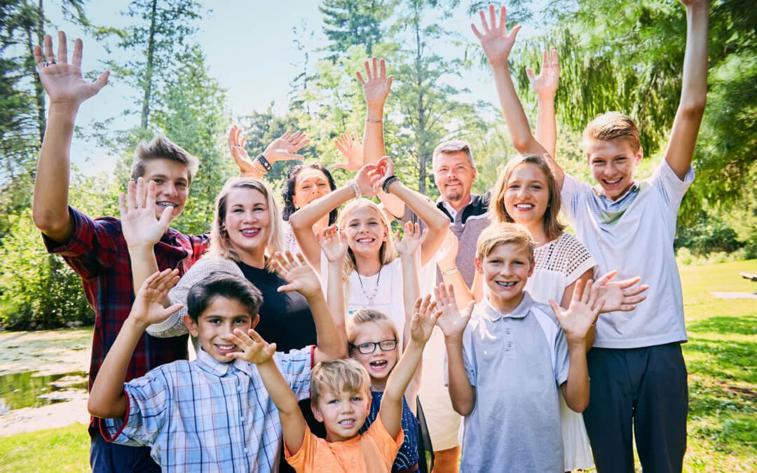 Portrait of happy blended family of eleven raising arms and laughing in park