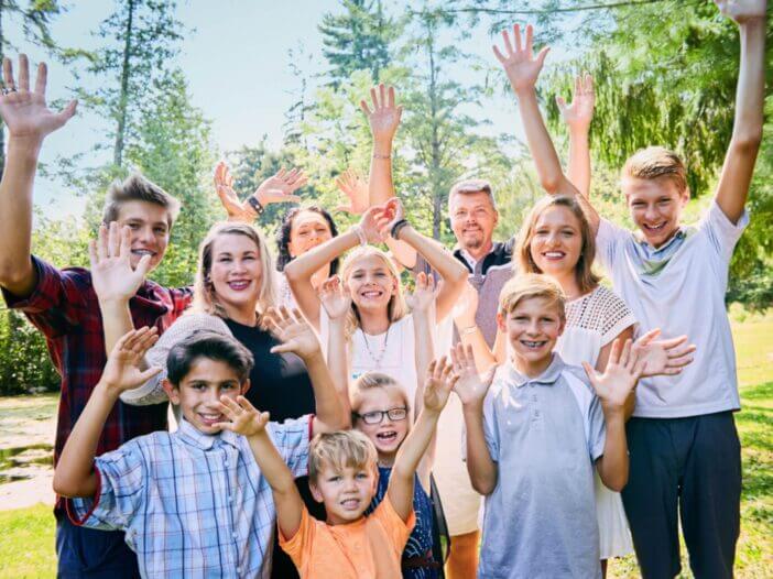 Portrait of happy blended family of eleven raising arms and laughing in park