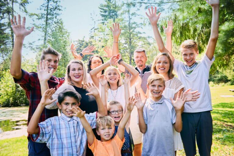 Portrait of happy blended family of eleven raising arms and laughing in park