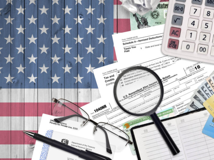 IRS form 1040NR Nonresident Alien Income tax return, calculator, and glasses lies flat on American flag