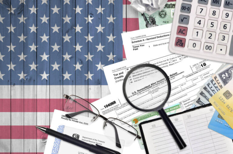 IRS form 1040NR Nonresident Alien Income tax return, calculator, and glasses lies flat on American flag