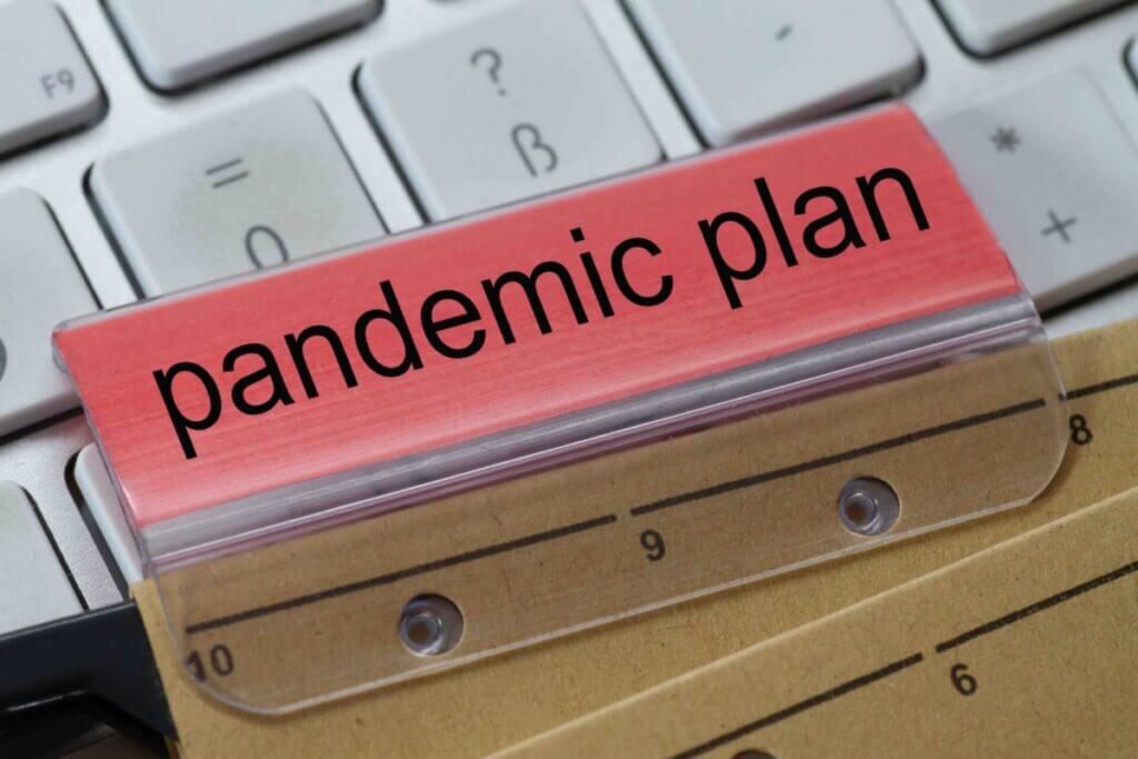 The words pandemic plan can be seen on the label of a brown hanging folder. The hanging folder is on a computer keyboard.