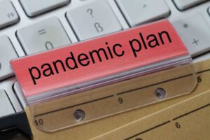 The words pandemic plan can be seen on the label of a brown hanging folder. The hanging folder is on a computer keyboard.