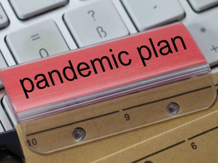 The words pandemic plan can be seen on the label of a brown hanging folder. The hanging folder is on a computer keyboard.