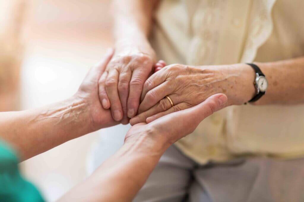 Nurse consoling her elderly patient by holding her hands