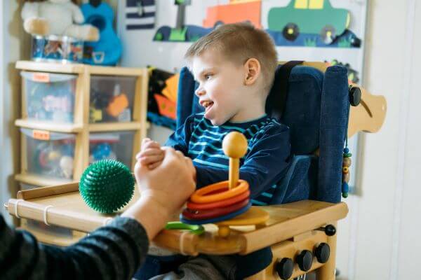 child with special needs in high chair with hand held in foreground