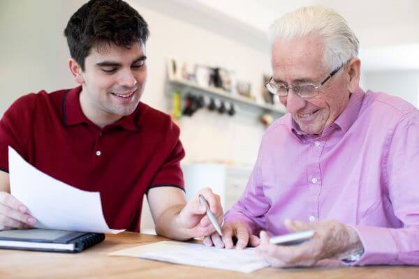 Son helps elder man with documents with pen in hand.