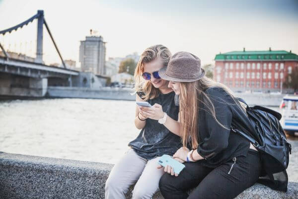 young adults look at a mobile phone at the edge of a waterway