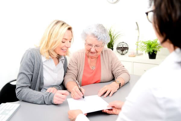 Smiling caregiver helps elder sign document