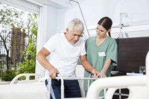 Nurse helps older man with walker in hospital room