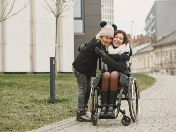 Mother with special needs in a wheelchair with her daughter embracing at park