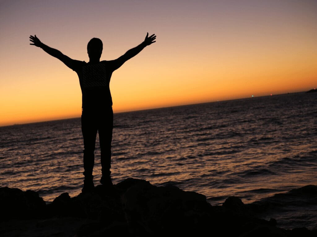 person in front of ocean standing with arms out wide