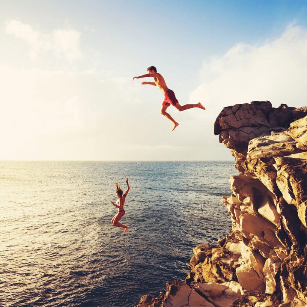 young couple leaps off rocky point into the ocean below