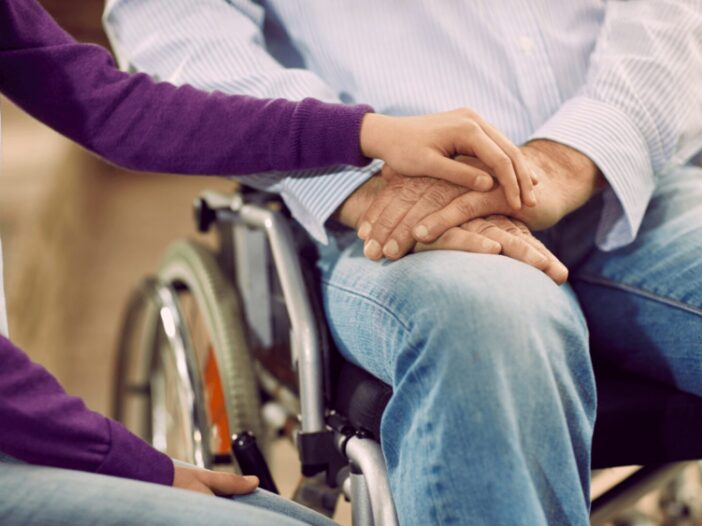 person in wheel chair holding hands with another person