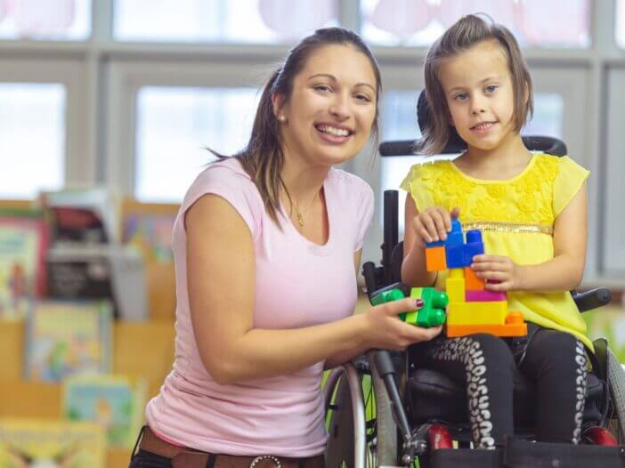 little girl in wheel chair playing with blocks with her caregiver