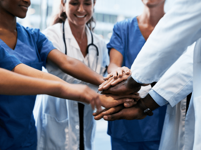 Medical professionals in a circle with their hands in