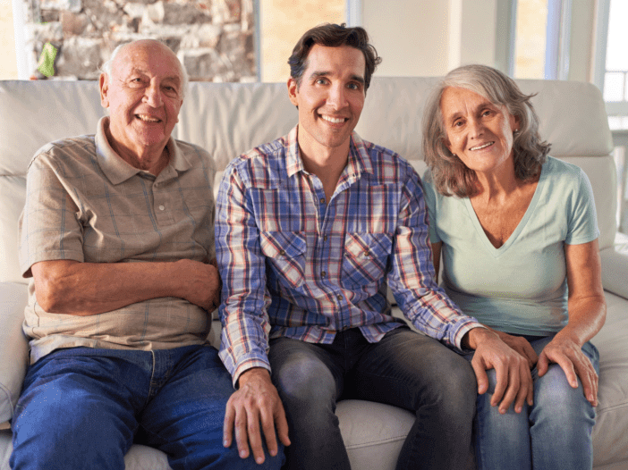 adult son sitting with aging parents on the couch