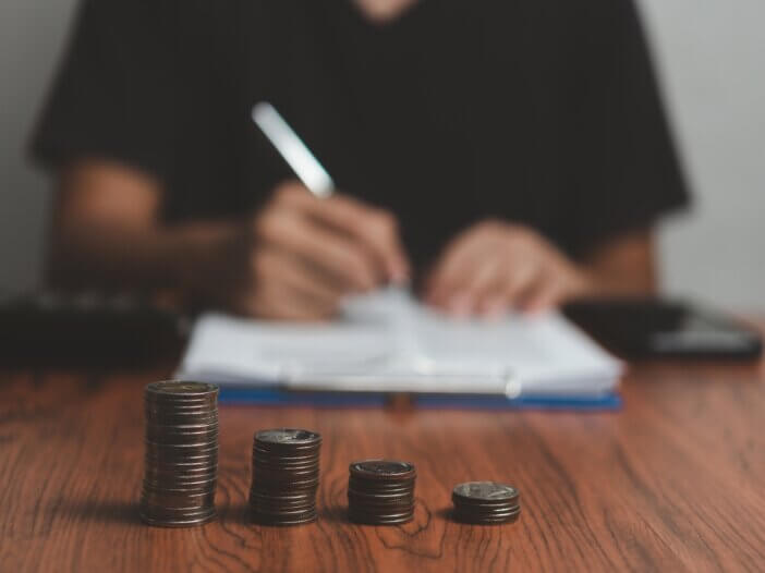 a guy paying off his debts filling out paperwork blurred in the background and there are a stack of coins focused in the image in front of him