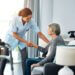a picture of an elderly woman on the couch at a long-term care facility and a nurse grabbing her hand to help her up